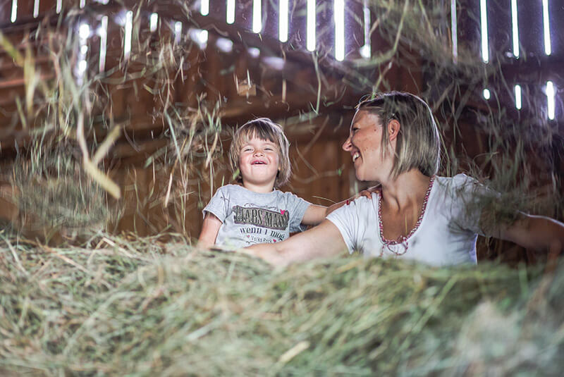 Madre e figlio siedono sul fieno e ridono insieme - Waidacherhof